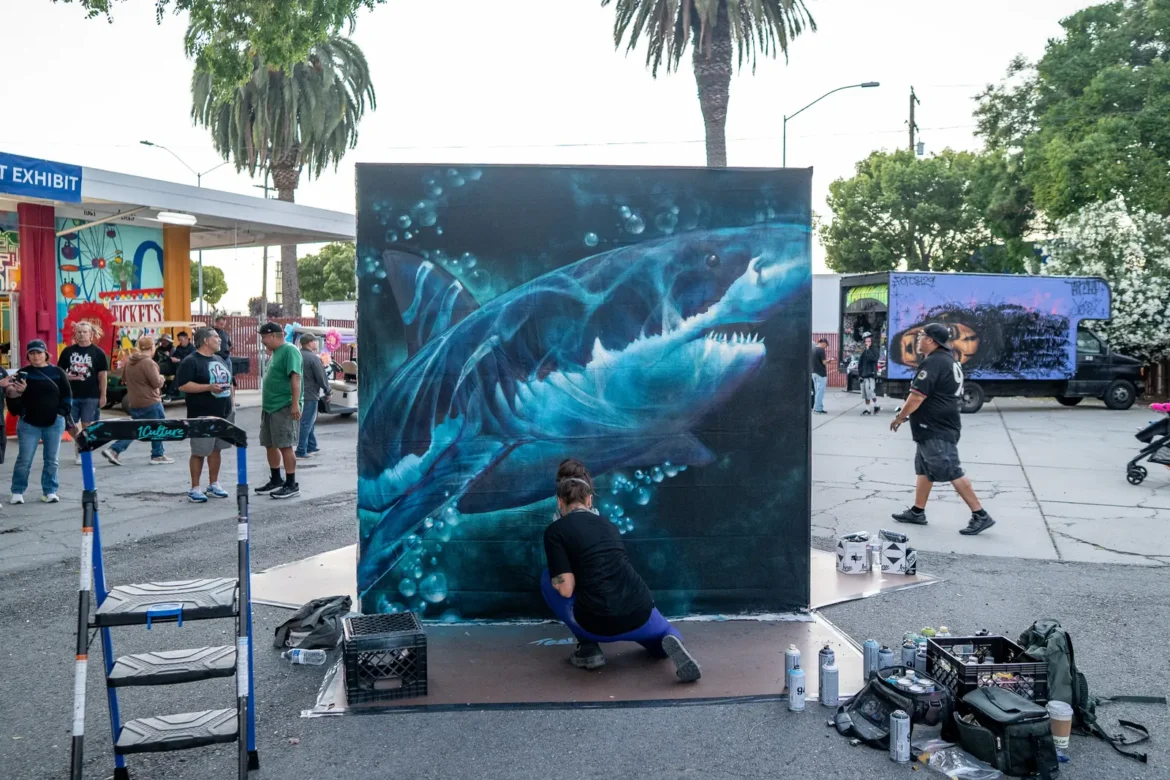 An artist works on a great white shark mural on the midway.