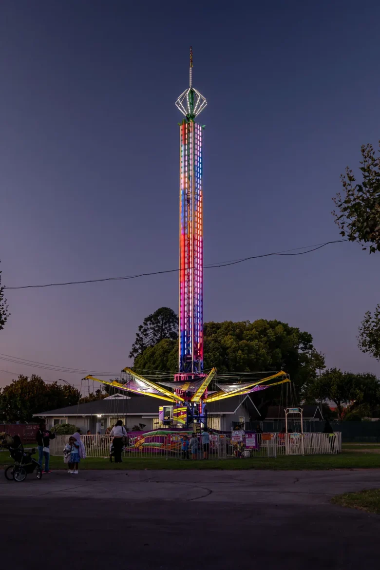 The drop tower stands tall over the fairgrounds at dusk.