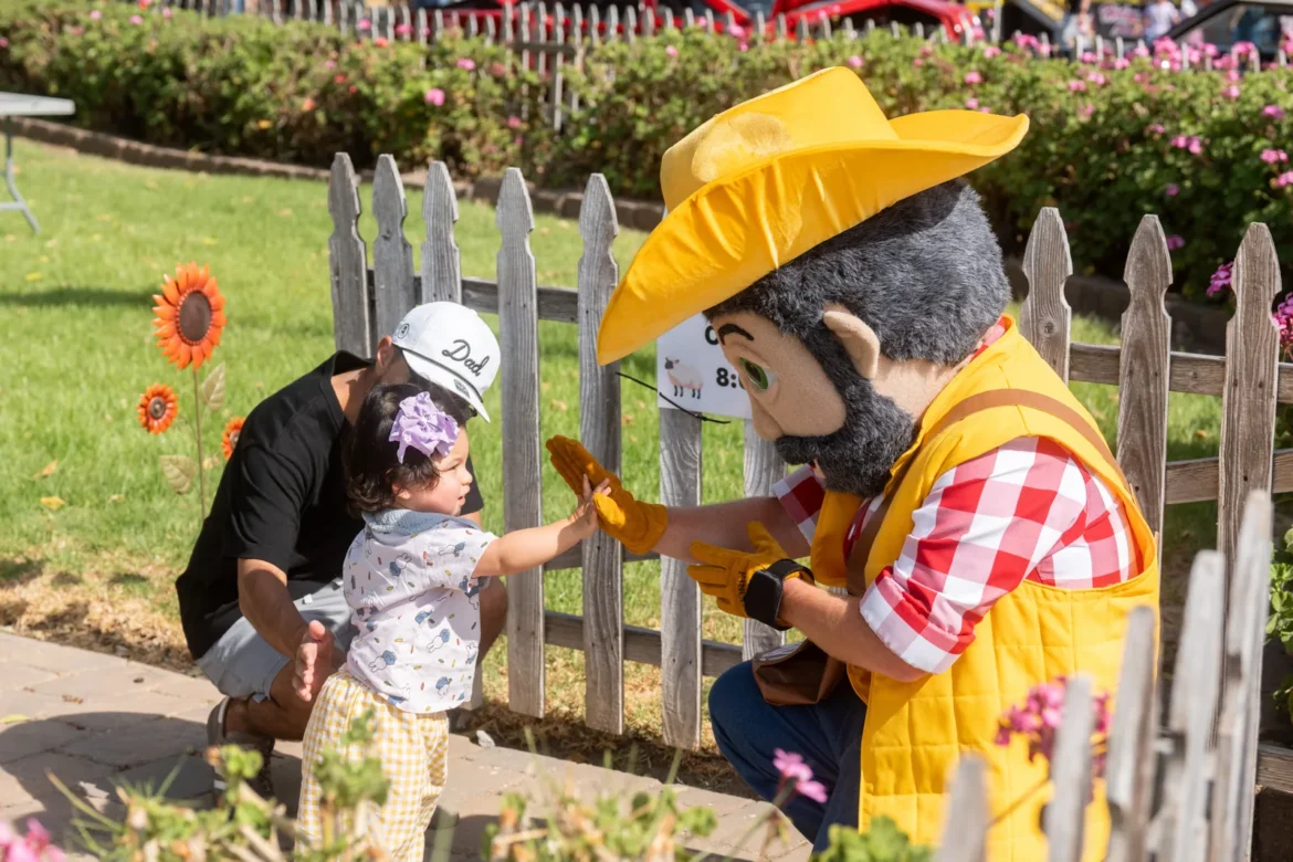 A toddler high-fives the Fair's cowboy mascot through the picket fence.