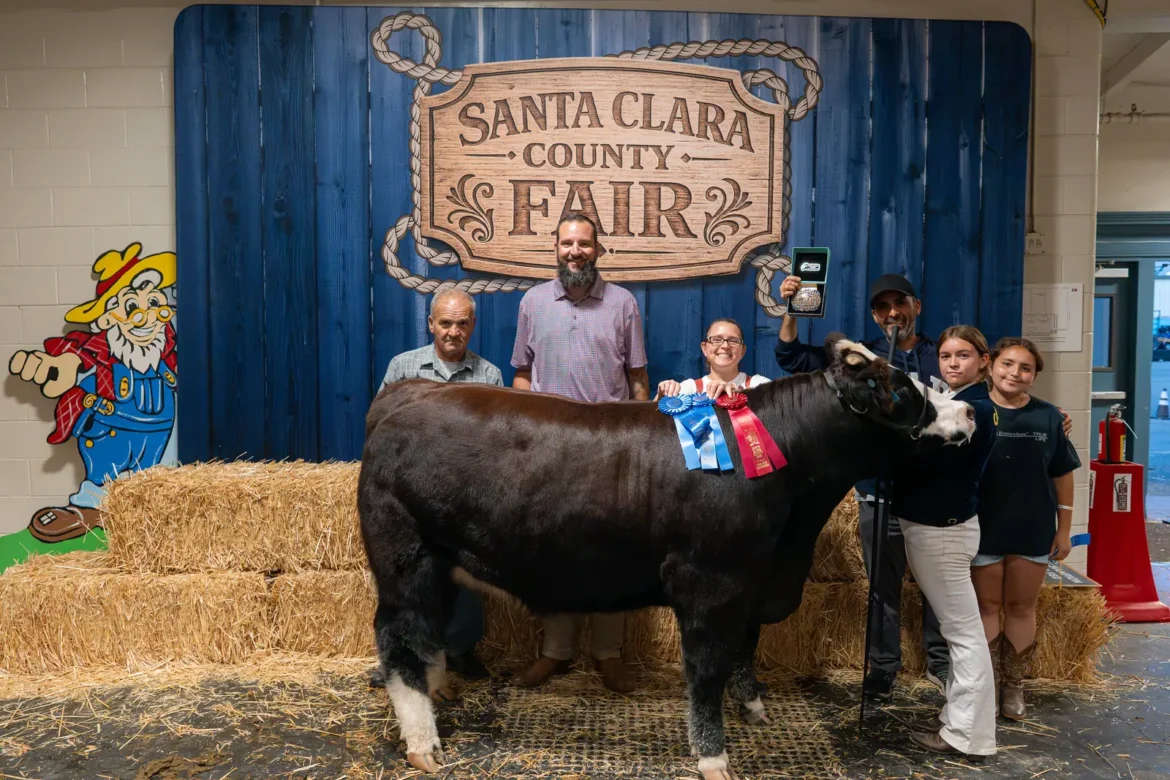 A champion steer and its exhibitor pose in front of the Fair backdrop.