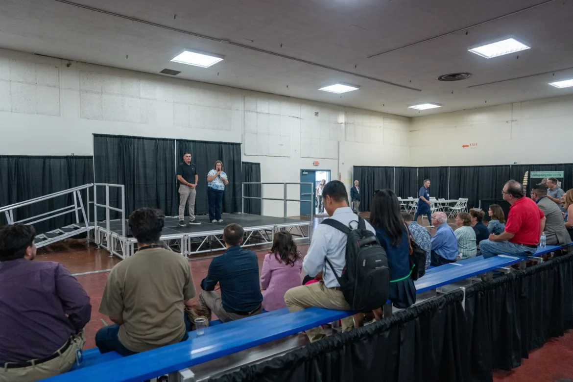 An audience gathers around the stage for an indoor presentation.