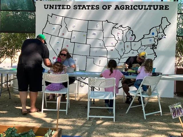 Children work at a craft table in front of the agriculture map.