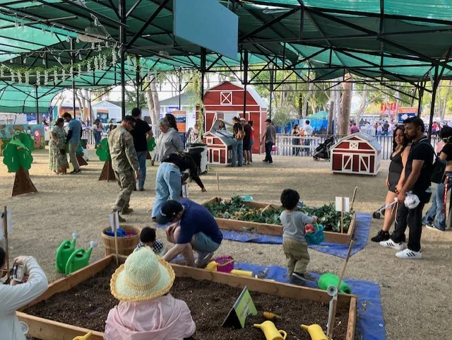 A child in a straw hat plants in a raised garden bed.